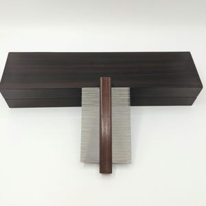 May include: A wooden box with a dark brown finish contains a silver comb with a wooden handle.