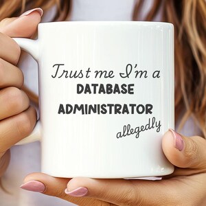 Könnte beinhalten: Eine weiße Keramiktasse mit schwarzem Text, der "Trust me I'm a DATABASE ADMINISTRATOR allegedly" lautet.