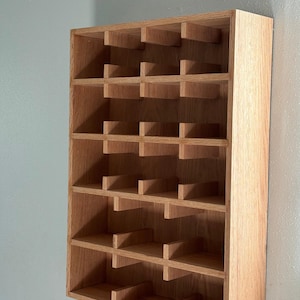 Puede incluir: Un botellero de madera para montaje en pared con m&uacute;ltiples compartimentos. El botellero es de madera clara y tiene forma rectangular. Est&aacute; dise&ntilde;ado para guardar botellas de vino, con cada compartimento dimensionado para una sola botella. Est&aacute; montado en una pared azul claro.