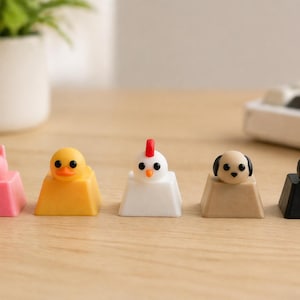Puede incluir: Una fila de cinco teclas de teclado con temática de animales. Las teclas presentan un cerdo rosa, un pato amarillo, una gallina blanca, un perro beige y un gato negro. Las teclas están sobre una superficie de madera.