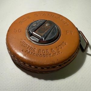 May include: An antique orange leather tape measure with the text "ROE STANDARD" and "JUSTUS ROE & SONS PATCHOGUE, N.Y." The tape measure is 50 ft. and has a metal center and a metal loop.