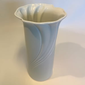 Könnte beinhalten: Eine hohe, hellblaue Keramikvase mit geriffeltem, gewelltem Rand. Die Vase hat ein glattes, geschwungenes Design auf der Vorderseite. Das Innere des Randes ist weiß. Diese dekorative Vase eignet sich zum Präsentieren von Blumen.
