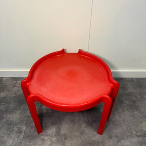 Puede incluir: Silla roja brillante de estilo moderno, con asiento circular y cuatro patas angulares. La silla tiene un perfil bajo y un diseño minimalista, adecuada para uso en interiores o exteriores.