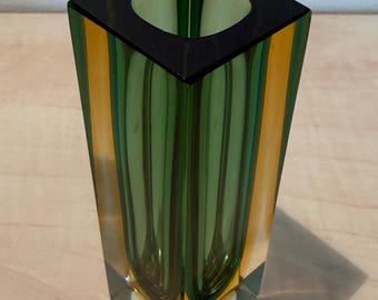 May include: A square-shaped glass vase with a black rim and a clear base. The vase features vertical stripes of green and orange. The interior is green, and the exterior has a glossy finish. The vase is a decorative item.
