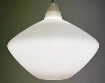 Puede incluir: Una lámpara colgante de vidrio esmerilado blanco. La lámpara tiene una pantalla ancha en forma de diamante y una parte superior cilíndrica. Un cable metálico suspende la lámpara del techo. La lámpara está iluminada, proyectando un brillo suave.
