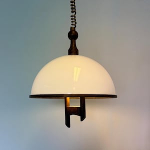 Könnte beinhalten: Eine weiße, kuppelförmige Pendelleuchte mit dunklem Holzakzent und passender Halterung. Die Leuchte hängt an einem spiralförmigen Kabel. Das Design ist schlicht und modern, passend für verschiedene Einrichtungsstile.