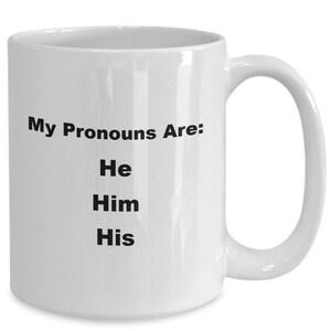 Puede incluir: Taza de café de cerámica blanca con el texto "My Pronouns Are: He Him His" impreso en negro.