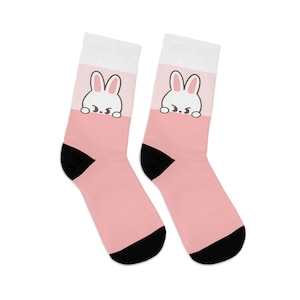 May include: A pair of pink and white socks with a cute cartoon bunny peeking out from behind the top of the sock. The bunny has black eyes and a small mouth.