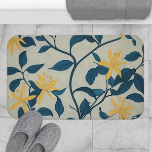 Könnte beinhalten: Ein rechteckiger Badteppich mit einem floralen Design aus gelben Blüten und dunkelblauen Blättern auf hellbeigem Hintergrund. Der Teppich liegt auf einem gefliesten Boden, mit einem Paar grauer Hausschuhe.