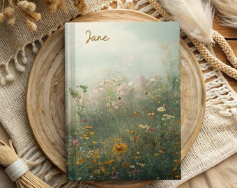 May include: A softcover journal with a floral design on the cover. The cover features a field of wildflowers in shades of pink, yellow, and white, with a soft, dreamy background. The name "Jane" is written in gold script at the top of the cover.