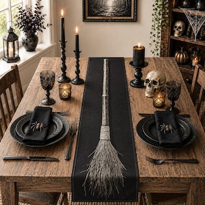 May include: A wooden broom with a textured handle and natural bristles centered on a black table runner. The table setting includes black plates, black napkins with spider napkin rings, black cutlery, black candles, and a skull decoration.
