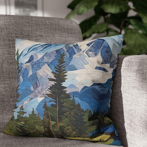 Può includere: Un cuscino blu e verde con un collage di montagne e alberi. Il cuscino è realizzato in tessuto e ha una consistenza morbida e confortevole.