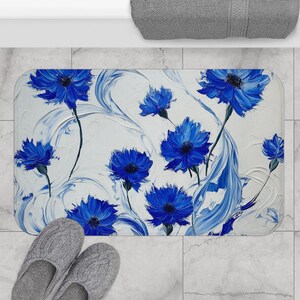 May include: A white bath mat with a blue floral design. The flowers are stylized and have a painterly look. The background is white with blue swirls.