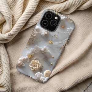 Könnte beinhalten: Smartphone-Hülle mit marmorähnlichem Design mit weißen Wolken, goldenen Sternen und einer Blume. Die Hülle hat einen hellgrauen Hintergrund und ein glänzendes Finish. Die Kameralinsen sind oben sichtbar.