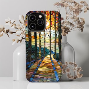 Könnte beinhalten: Eine Handyhülle aus Buntglas mit einem farbenfrohen Design aus Bäumen und einem Weg, der in einen Wald führt. Die Hülle hat einen schwarzen Rand und einen Ausschnitt für die Kamera.