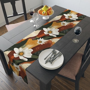 Puede incluir: Un camino de mesa floral marrón, verde y blanco con un diseño abstracto moderno. El camino de mesa está colocado sobre una mesa de madera oscura con un plato blanco y cubiertos.