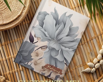 May include: A white journal with a floral design featuring a large gray flower and smaller white flowers. The text "Marianne" is written on the cover.