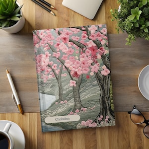 以下が含まれることがあります： グレーの背景にピンクの桜の花が咲いた花柄のパーソナライズされたノート。表紙には「クリスティーナ」という名前が印刷されています。