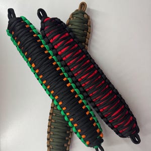 Può includere: Quattro cordini da polso in paracord fatti a mano in nero, verde, rosso e marrone. Il cordino nero ha accenti verdi e arancioni. Il cordino rosso ha accenti neri. I cordini verdi e marroni hanno accenti marroni. Ogni cordino ha un anello in alto.
