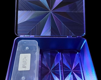 May include: Open, iridescent blue case with geometric starburst pattern on the inside. A clear plastic container with the text "NAD+1" is inside the case. The case has a black background.