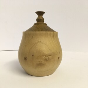 Peut inclure: Une boîte en bois avec un couvercle, la boîte est de couleur brun clair et le couvercle est en bois brun foncé. La boîte a une forme arrondie et une finition lisse.