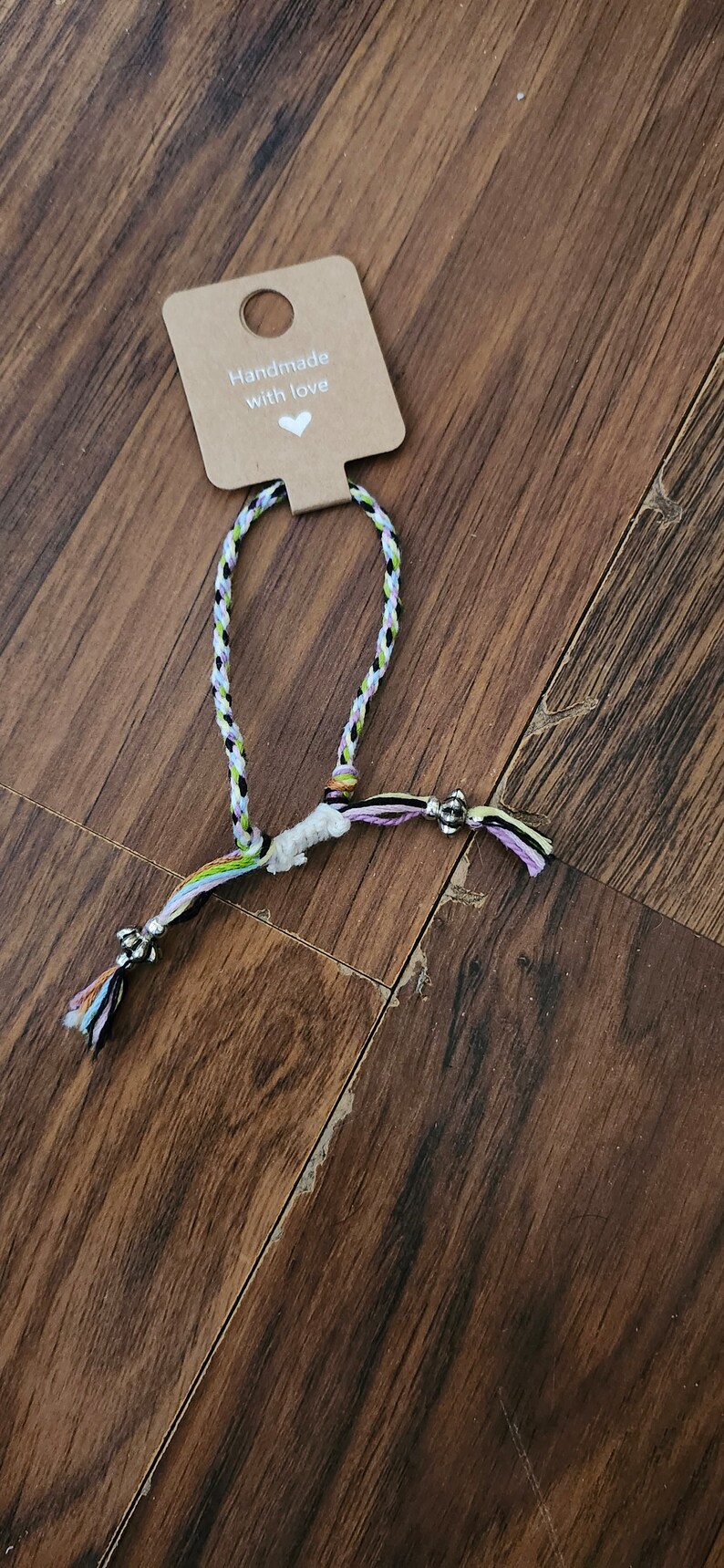 May include: A multi-colored braided bracelet with silver beads and a tag that says "Handmade with love".
