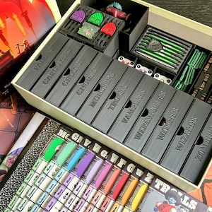 Peut inclure: Un organisateur de jeu de société avec des compartiments étiquetés pour divers composants de jeu. Les boîtes noires sont étiquetées avec des noms de créatures fantastiques. Des plateaux et des cartes de jeu colorés sont visibles, ainsi que des pièces et des figurines.