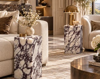 May include: Two rectangular side tables crafted from white marble with prominent dark purple veining. Each table features a smooth, polished finish and a solid block structure, positioned as functional furniture pieces in a living room setting.