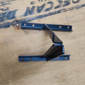 May include: Black metal shelf bracket with two horizontal pieces and a vertical piece that connects them. The bracket is designed to be mounted to a wall.