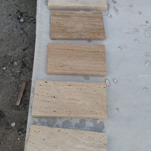 May include: Six rectangular tiles of travertine stone, arranged in a row from top to bottom. The tiles are various shades of beige and brown, with a natural, textured surface.