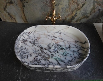 May include: Oval-shaped marble sink with a white background and purple and gray veining. The sink is on a dark gray surface.