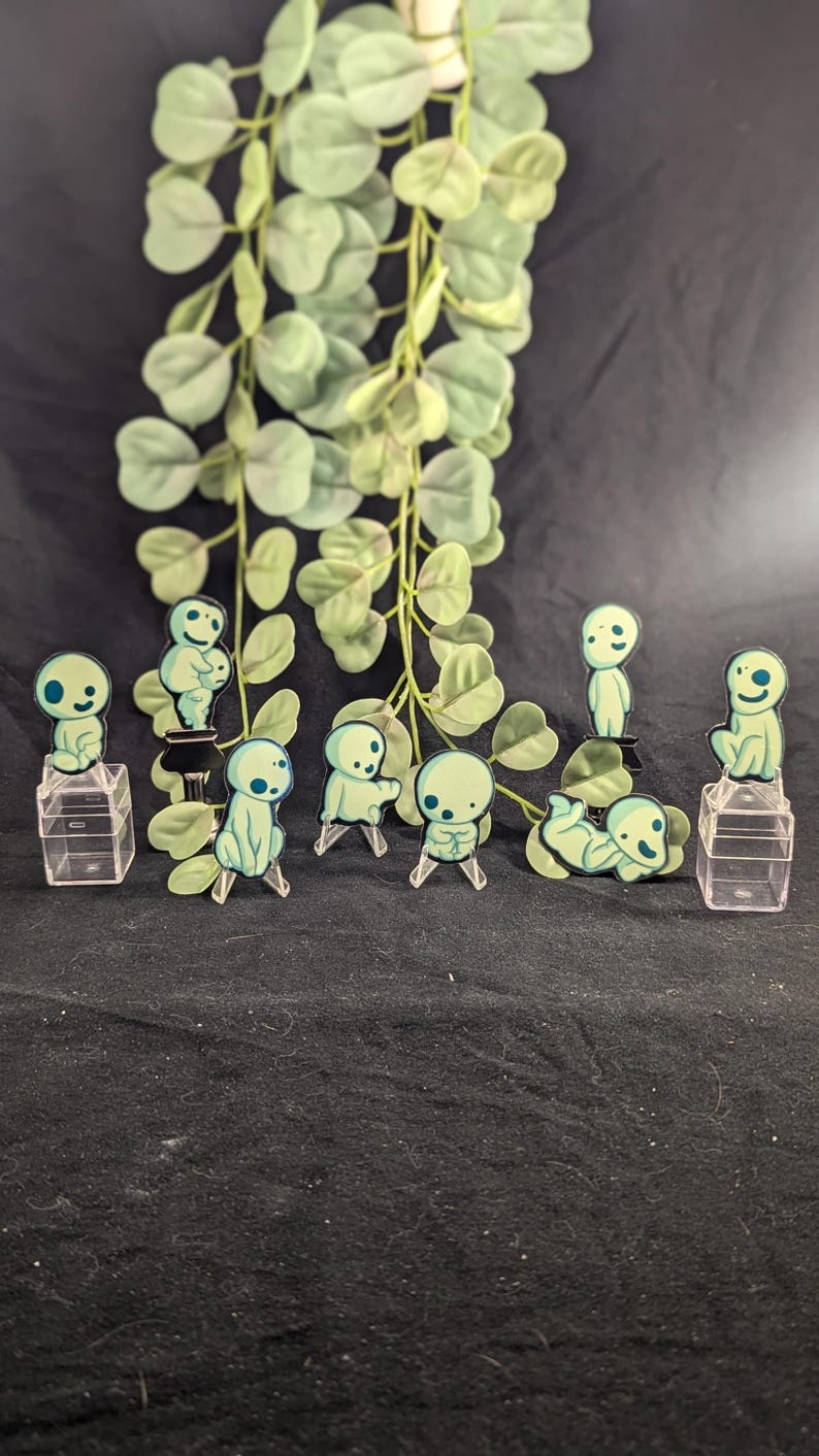 May include: Eight green and blue cartoon characters on clear plastic stands. The characters are all different poses and are reminiscent of the characters from the movie "My Neighbor Totoro".