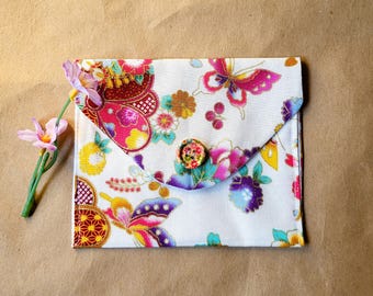 May include: A white fabric envelope with a colourful floral and butterfly print. The envelope has a flap that closes with a single button.