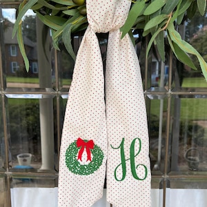 May include: A white fabric door swag with red polka dots. The swag is decorated with a green embroidered wreath with a red bow and the letter "H" in green.