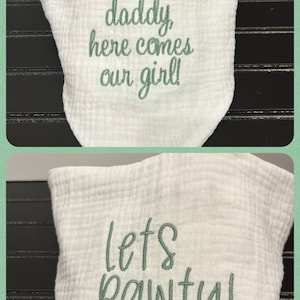 Pu&ograve; includere: Bavaglino in cotone bianco con ricamo verde. Un lato dice "Pap&agrave;, ecco la nostra bambina!" e l'altro lato dice "Facciamo festa!"
