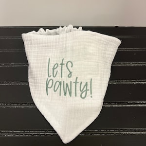 Pu&ograve; includere: Bavaglino bandana bianco con ricamo verde che dice "Let's Pawty!"