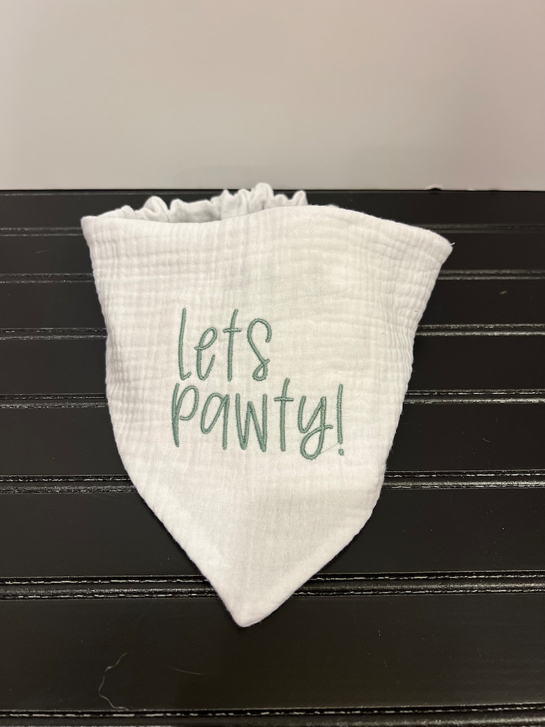 Pu&ograve; includere: Bavaglino bandana bianco con ricamo verde che dice "Let's Pawty!"