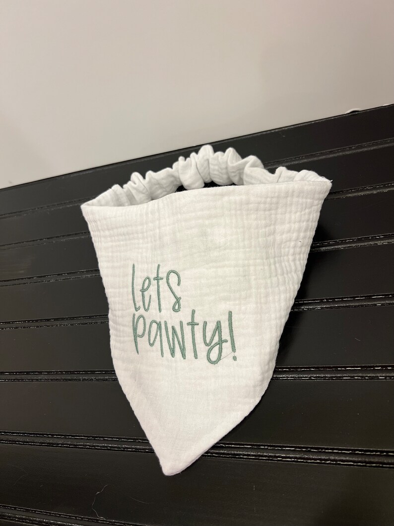 Pu&ograve; includere: Bandana bianca con un messaggio ricamato in verde che dice "Let's Pawty!"