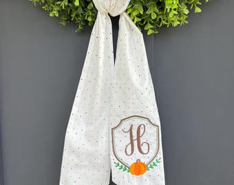 May include: White fabric door hanger with a repeating pattern of small red and brown dots. The bottom of the hanger has a decorative embroidered patch with the letter "H", a pumpkin, and green leaves.