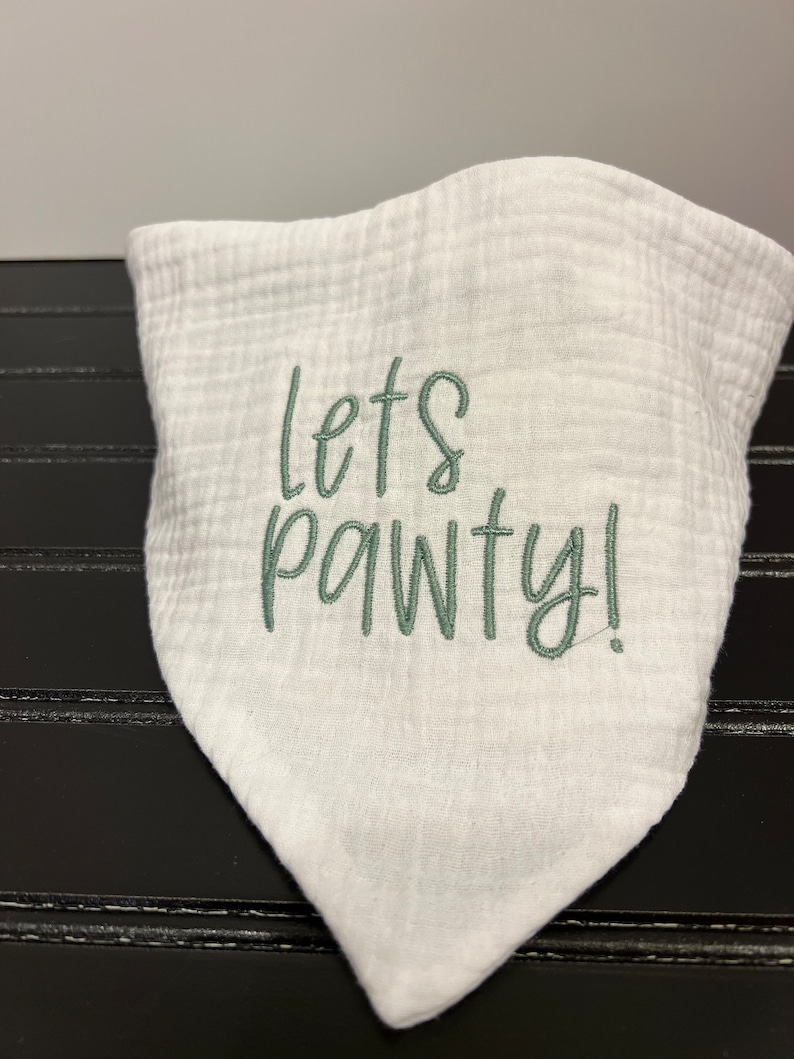 Pu&ograve; includere: Bandana di cotone bianco con ricamo verde che dice "Let's Pawty!"