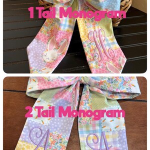 K&ouml;nnte beinhalten: Oster-Stoffschleife mit Patchwork-Design in Pastellfarben. Die Schleife hat ein Hasen- und Blumenmuster mit gestickten Monogrammen. Der Text "1 Tail Monogram" und "2 Tail Monogram" sind sichtbar.
