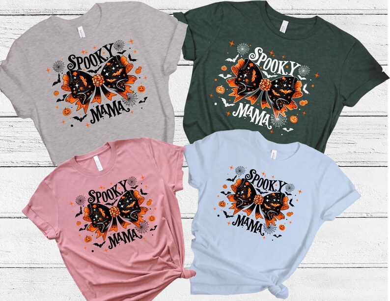 May include: Four t-shirts in grey, green, pink, and light blue. Each shirt displays a Halloween graphic with a black bow, bats, pumpkins, and the words "Spooky Mama".