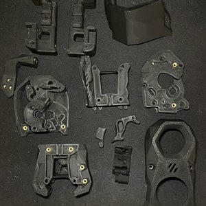 May include: A set of 12 black 3D printed parts for a project. The parts are various shapes and sizes, with some having small gold screws.