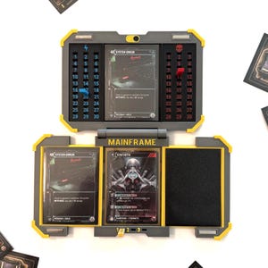 May include: A gray and yellow Mainframe card holder, open to display cards. The holder has numbered slots and a skull icon. The cards feature text and graphics, including "System Error" and "Synthetix".