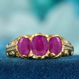 May include: A gold ring with three round ruby stones set in a decorative band.