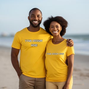 May include: Two people wearing matching yellow t-shirts with the text "YOUR DESIGN HERE" in a black outlined font. The couple is smiling and standing on a beach. The man is wearing khaki pants and the woman is wearing yellow pants.