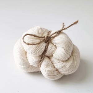 Puede incluir: Un ovillo de hilo blanco atado con cuerda, listo para tejer o hacer ganchillo.