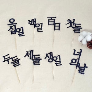 May include: Black and white Korean language word cutouts on sticks. The words are "오늘", "별", "꿈", "첫돌", "세돌", "생일", "너", "두돌".
