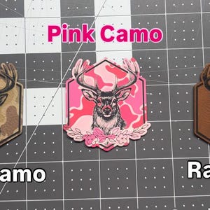 May include: Three decorative patches with deer designs. One features a deer head on a duck camo background, another on a pink camo background, and the last on a rawhide background. The text "Pink Camo", "Duck camo", and "Rawhide" are displayed.