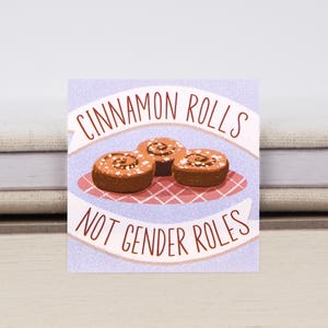 Könnte beinhalten: Quadratische Grafik mit dem Text "CINNAMON ROLLS NOT GENDER ROLES" über und unter einer Illustration von drei Zimtschnecken auf einem Teller mit rot-weißem Karomuster.